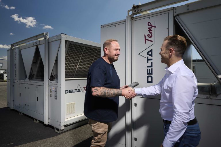 Technieker werkt aan een Delta-Temp koelinstallatie op een bedrijfsterrein, met servicewagen op de achtergrond.