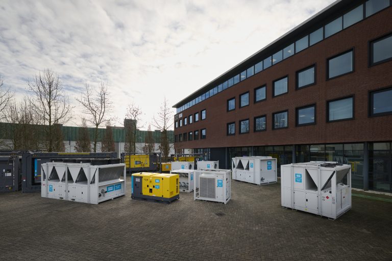 Verschillende witte chillers, airhandlers en generator van Atlas Copco Rental opgesteld op bij een kantoorgebouw.
